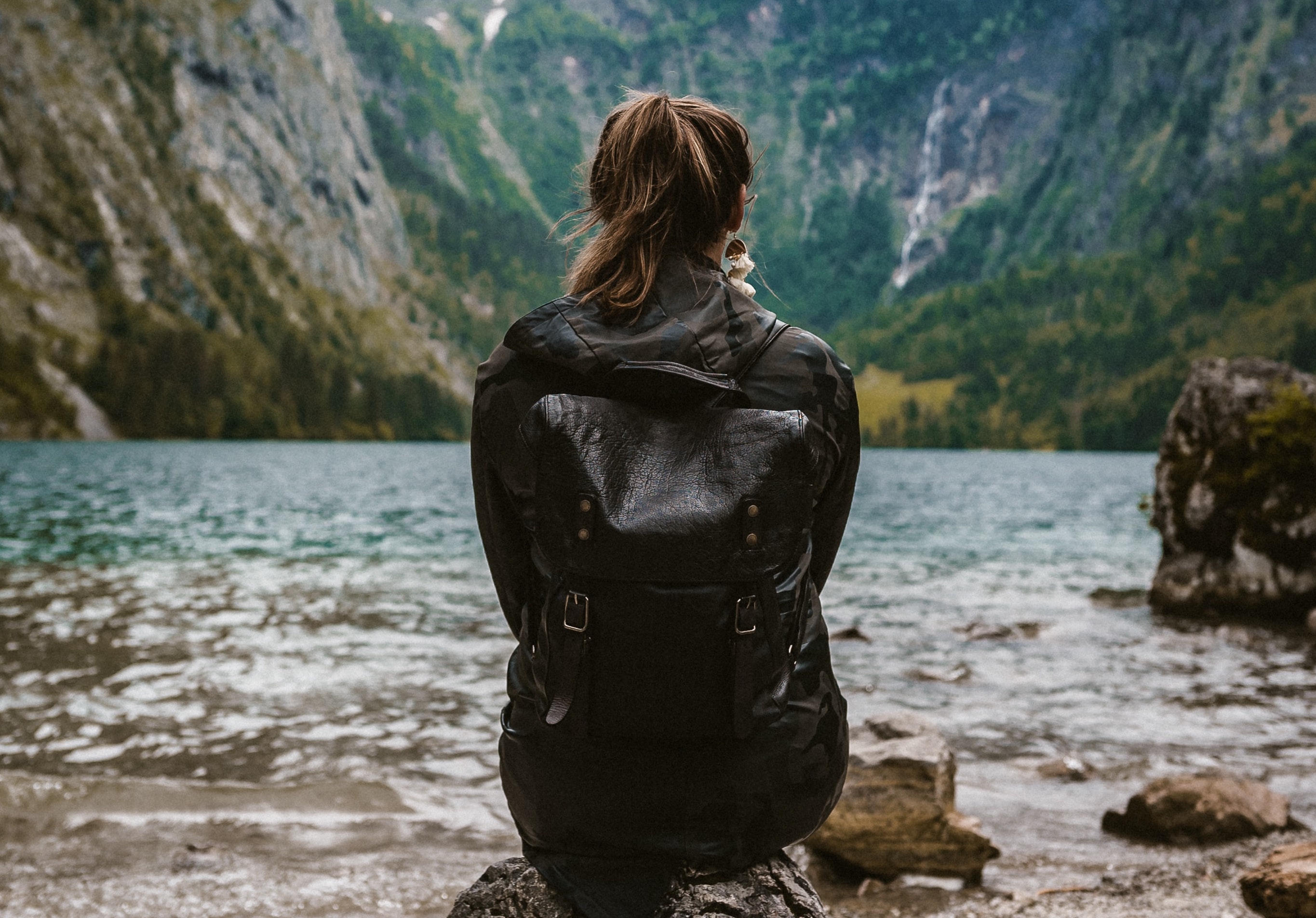 woman sitting on a rock looking at water and mountains